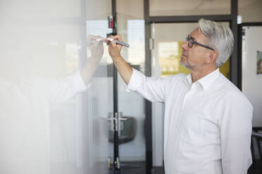 Mature businessman writing on whiteboard in office - RBF08384