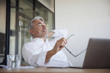 Mature businessman holding eyeglasses relaxing with eyes closed in office - RBF08396