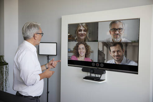 Älterer Geschäftsmann im Gespräch über Videokonferenz durch Fernsehen im Büro - RBF08399