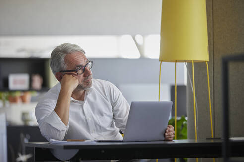 Geschäftsmann mit Laptop, der am Arbeitsplatz nachdenkt - RBF08414