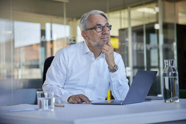 Älterer Geschäftsmann mit Laptop, der am Arbeitsplatz nachdenkt - RBF08418