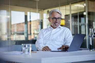 Lächelnder Geschäftsmann bei der Arbeit am Laptop im Büro - RBF08422
