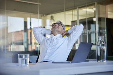 Smiling businessman relaxing while sitting on chair at workplace - RBF08424