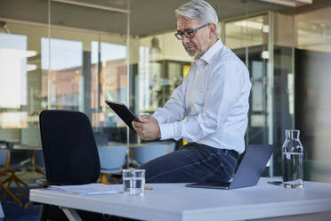 Businessman working on tablet PC while sitting on desk in office - RBF08429