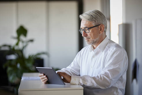 Älterer Geschäftsmann arbeitet an einem Tablet-PC am Schalter im Büro - RBF08430