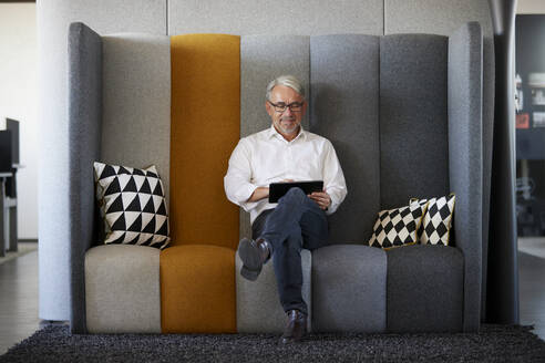 Lächelnder Geschäftsmann mit Tablet-PC auf dem Sofa im Büro - RBF08435