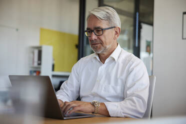 Geschäftsmann arbeitet am Laptop am Schreibtisch im Büro - RBF08439