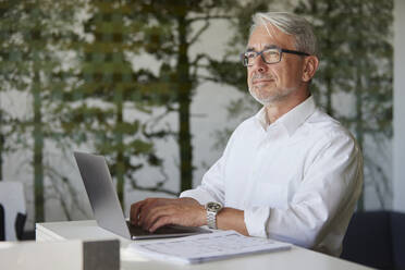 Geschäftsmann beim Nachdenken über die Arbeit am Laptop im Büro - RBF08453