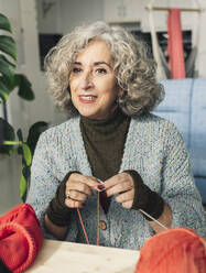 Senior woman knitting and sewing in living room - JCCMF04753