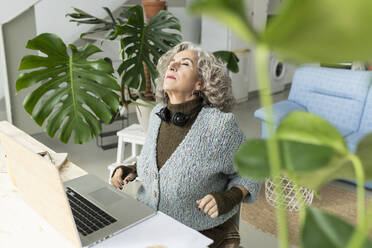 Älterer Freiberufler mit Laptop, der sich im Heimbüro entspannt - JCCMF04758