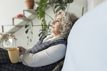 Nachdenkliche ältere Frau mit Kaffeetasse, die sich zu Hause entspannt - JCCMF04776