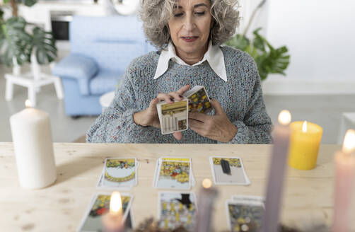 Ältere Frau liest Tarotkarten auf dem Tisch zu Hause - JCCMF04780