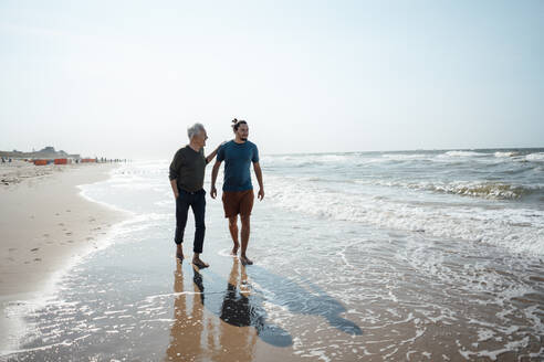 Vater und Sohn gehen zusammen auf nassem Sand am Strand spazieren - GUSF06563