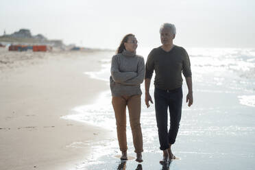 Daughter with arms crossed walking with father at beach - GUSF06567