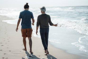 Älterer Mann gestikuliert mit seinem Sohn beim gemeinsamen Spaziergang am Strand - GUSF06570