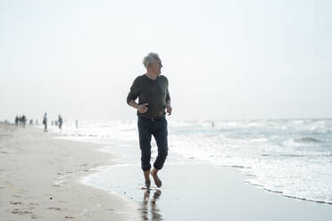 Senior man looking at sea walking at beach - GUSF06576