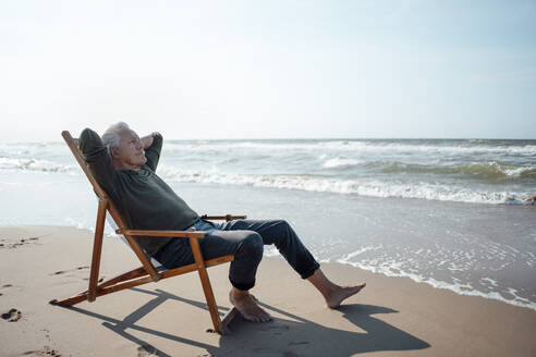 Senior man relaxing on chair by seashore at beach - GUSF06577