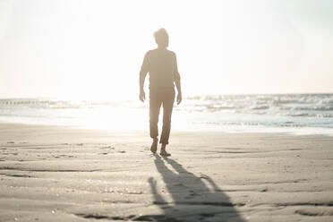 Älterer Mann spaziert am Strand an einem sonnigen Tag - GUSF06582