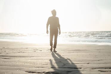 Senior man walking at beach on sunny day - GUSF06582