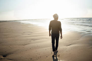 Senior man walking towards sea at beach - GUSF06585