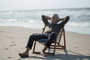 Senior man relaxing on chair at beach - GUSF06593