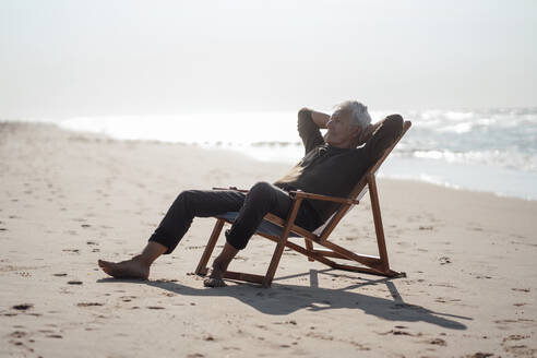 Mann entspannt mit Händen hinter dem Kopf am Strand - GUSF06595