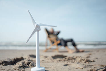 Modell einer Windkraftanlage auf Sand mit einem älteren Mann im Hintergrund - GUSF06599