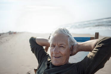 Lächelnder Mann entspannt sich auf einem Stuhl am Strand - GUSF06602