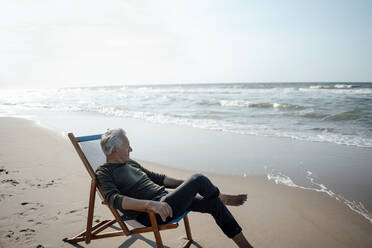 The boy is sitting on a folding chair on the shore of a lake or river.  Recreation, weekends, tourism. Rear view - a Royalty Free Stock Photo from  Photocase