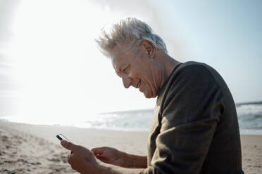 Lächelnde ältere Frau mit Smartphone am Strand - GUSF06607