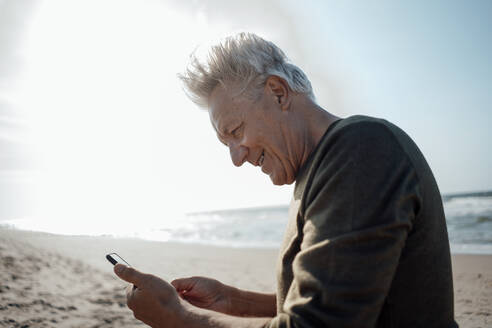 Lächelnde ältere Frau mit Smartphone am Strand - GUSF06607