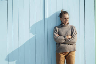 Woman with arms crossed leaning on blue door - GUSF06615