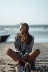 Young woman sitting on wooden post at beach - GUSF06624