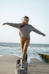 Junge Frau balanciert auf Holzpfosten am Strand - GUSF06627