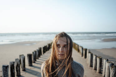 Ernste Frau in der Nähe von Holzpfosten am Strand - GUSF06630