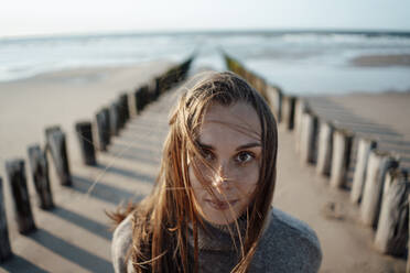 Junge Frau in der Nähe von Holzpfählen am Strand - GUSF06631