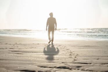 Älterer Mann geht an einem sonnigen Tag am Strand in Richtung Meer - GUSF06634