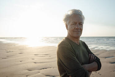 Älterer Mann lächelnd mit verschränkten Armen am Strand - GUSF06642