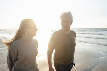 Lächelnde Frau mit Vater beim Spaziergang am Strand an einem sonnigen Tag - GUSF06643