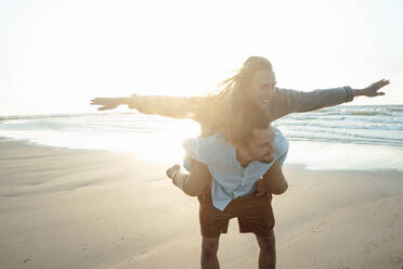 Man piggybacking woman at beach - GUSF06648