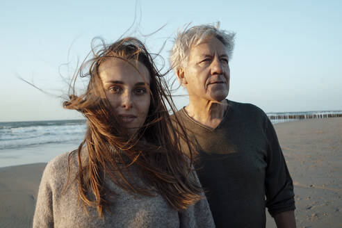 Tochter mit vom Wind zerzaustem Haar steht mit Vater am Strand - GUSF06653