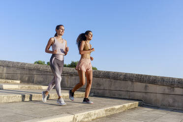 Smiling girl jogging with mother on steps - RFTF00148