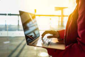 Anonymer Tourist tippt auf einer modernen Netbook-Tastatur, während er in einem modernen Flughafen-Terminal mit hellem Sonnenlicht und Fenstern vor dem Abflug sitzt - ADSF32567