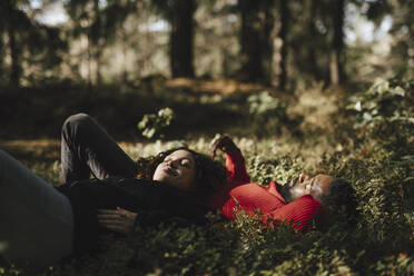 Schwangere Frau entspannt sich, während sie mit ihrem Freund auf Pflanzen im Wald liegt - MASF27196