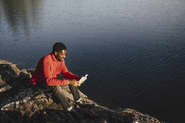 Man reading book while sitting on rock during weekend - MASF27215