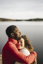 Heterosexual couple embracing by lake on sunny day - MASF27219