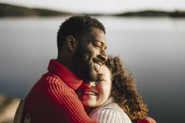 Happy couple embracing by lake on sunny day - MASF27220