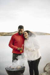 Happy woman preparing food with boyfriend against lake - MASF27222