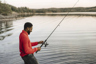 Smiling man fishing in lake during sunset - MASF27223