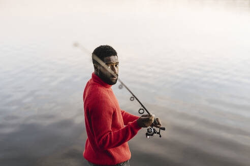 Man holding fishing rod at lakeshore during sunset - MASF27224